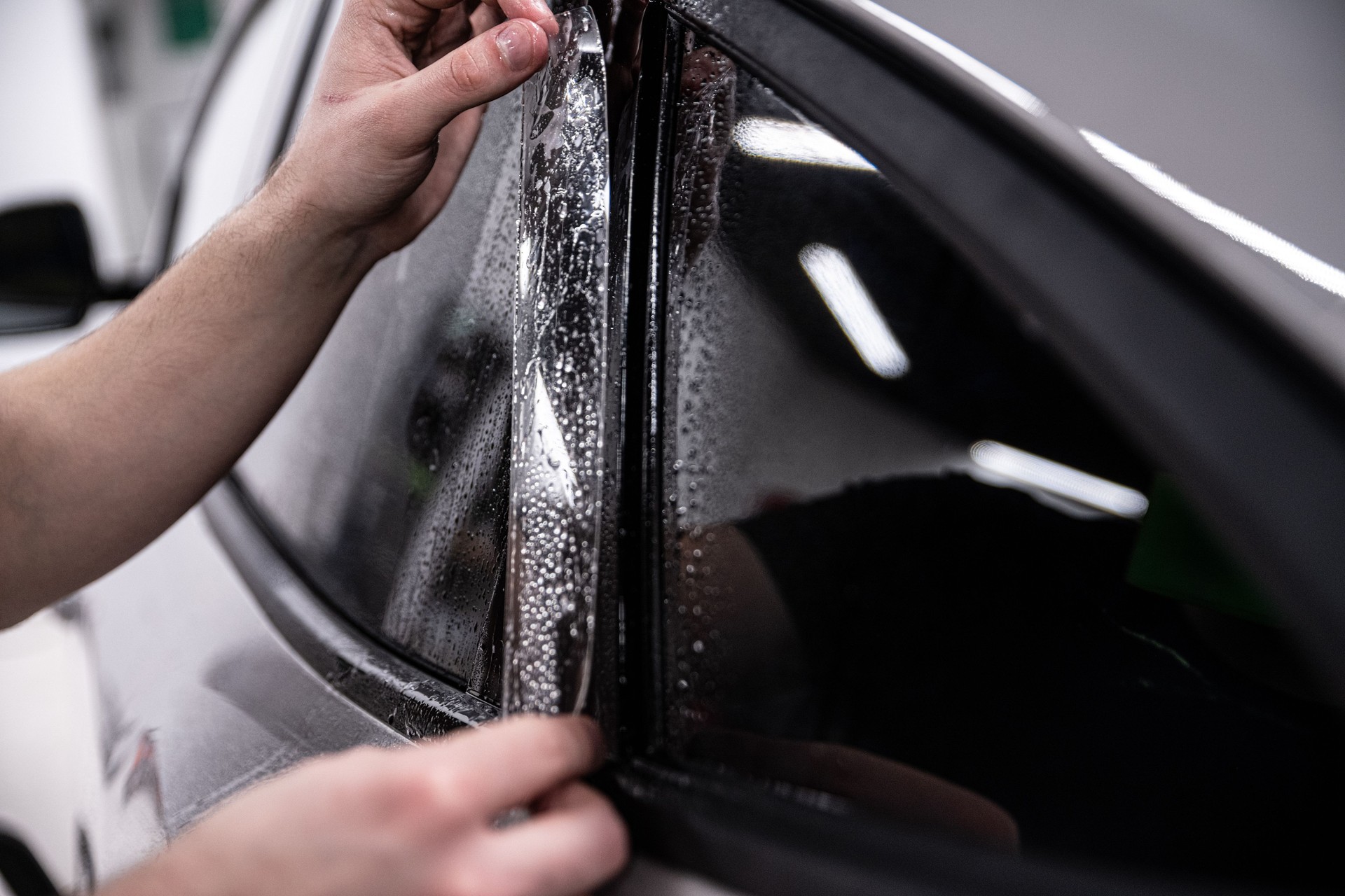 Employee of a car wash or a car detailing studio applies a colorless PPF protective film